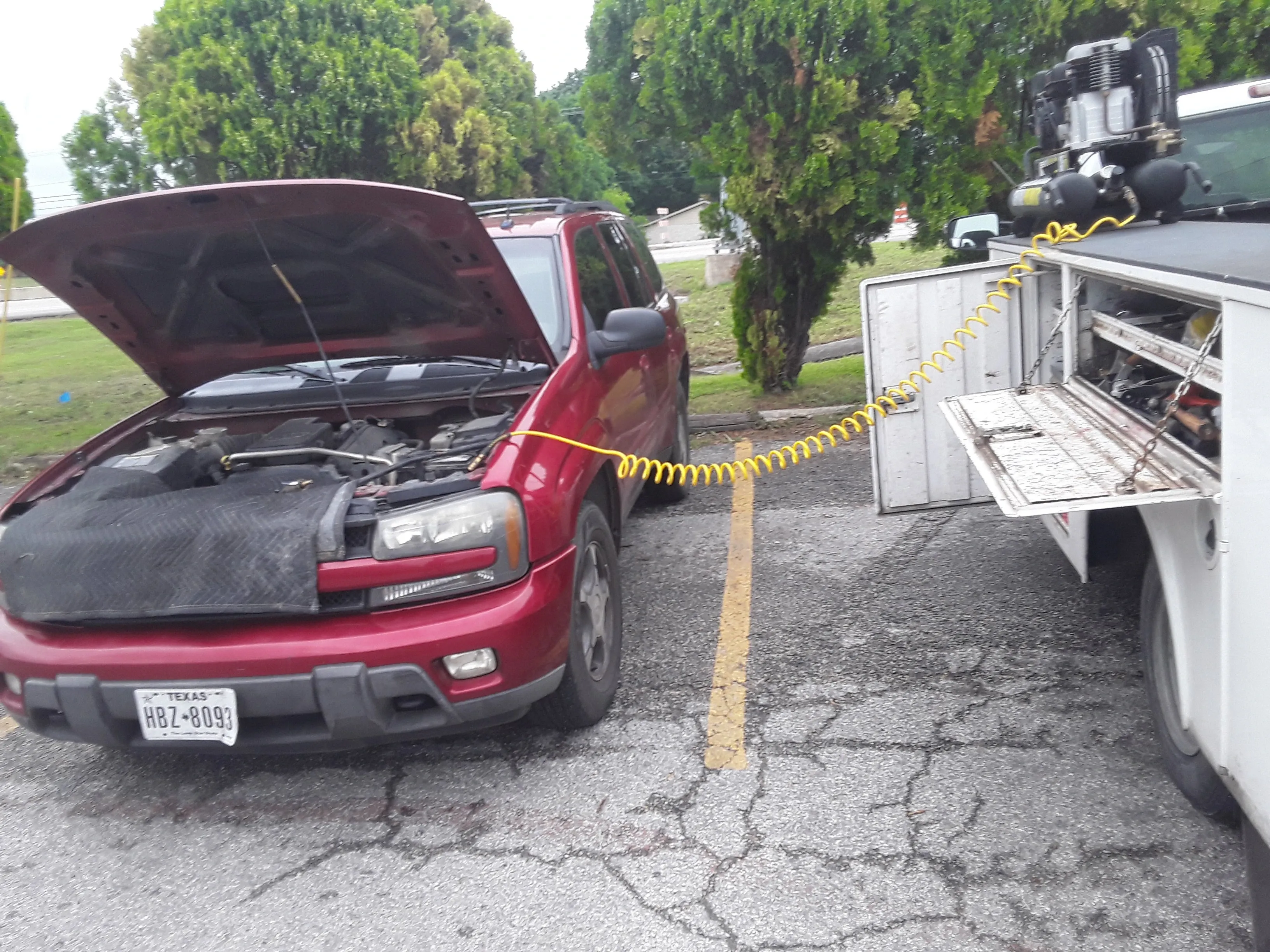 Red SUV connected to a yellow diagnostic cable or power cord in a parking lot.