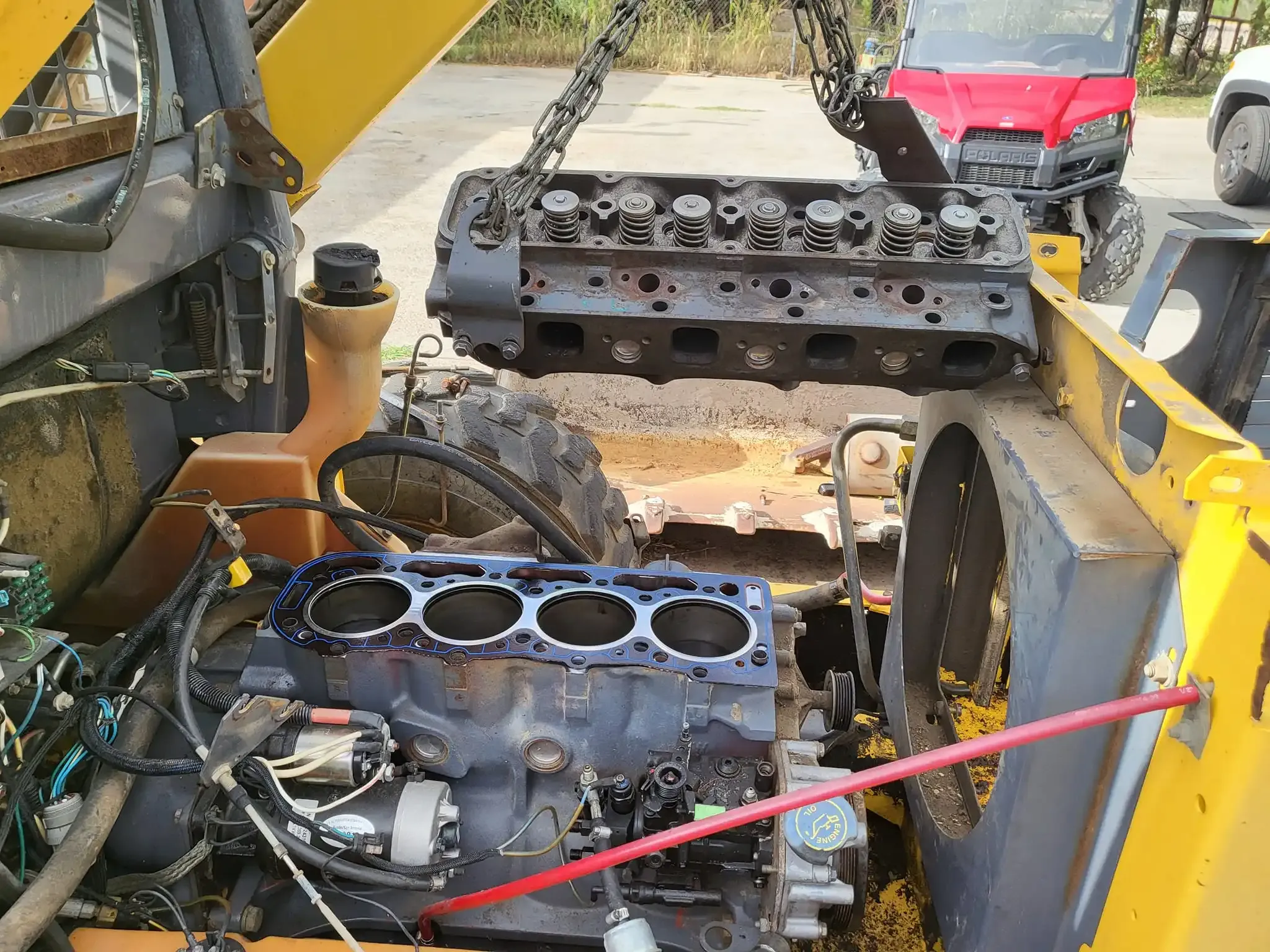 Heavy equipment engine head being lifted by a crane in an outdoor setting.