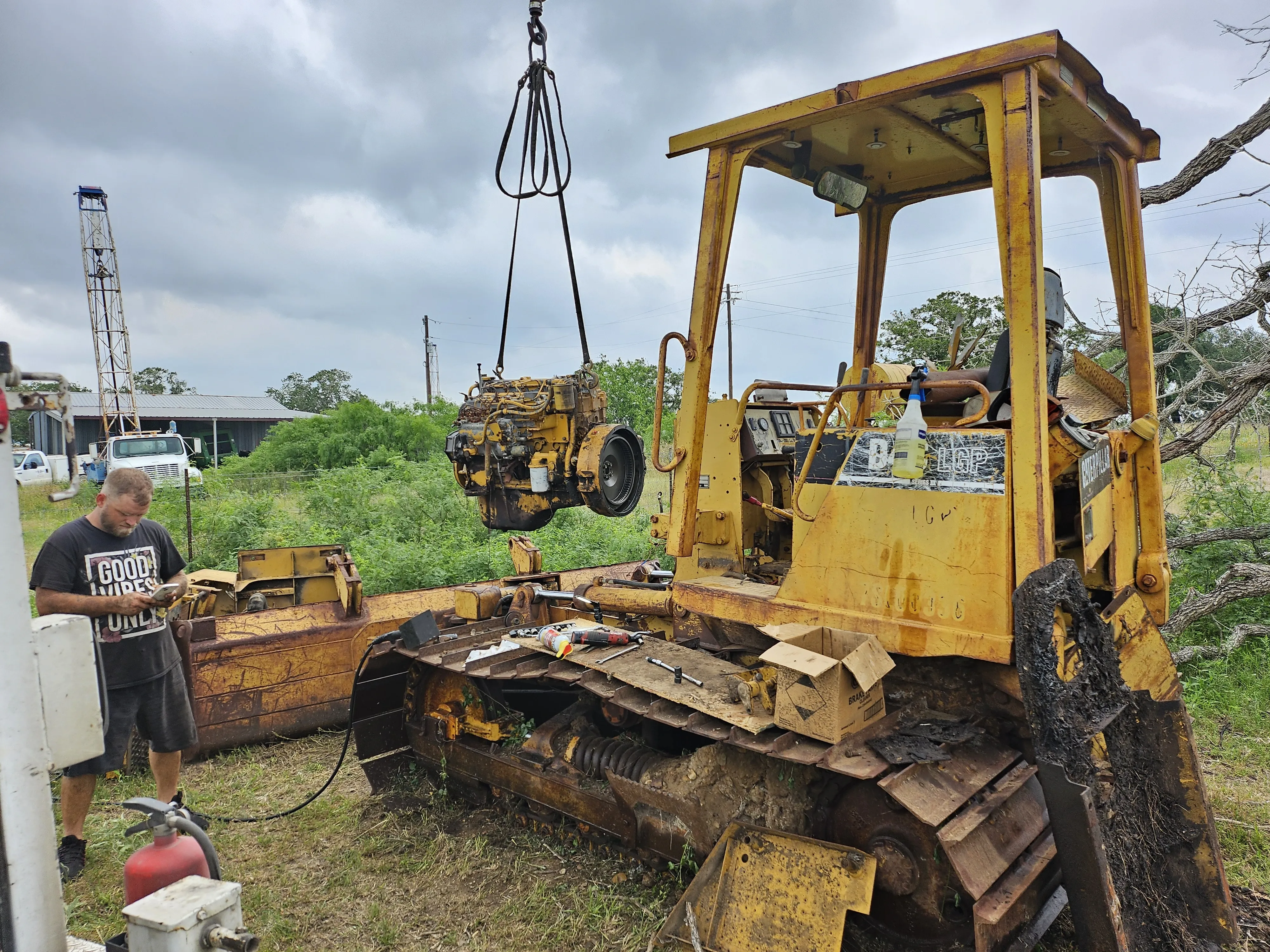 Skid steer engine block being lifted by a crane in an outdoor settiing.